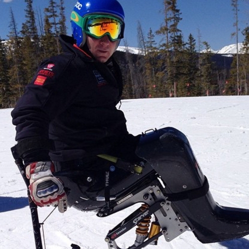 Andy Trollope on his skis, tree lined snow in the background and bright blue sky