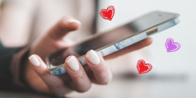 A woman's hand is holding a mobile phone with pink and purple hearts around it