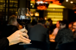a person holding a glass of wine, in their hand with a busy bar in the background