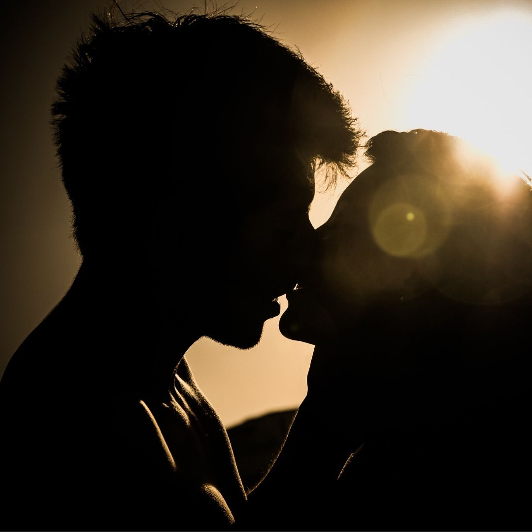 A couple are kissing silhouetted against a light