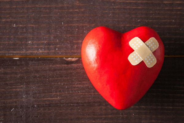 A red 3D heart with two plaster in a cross-shape on a wooden background