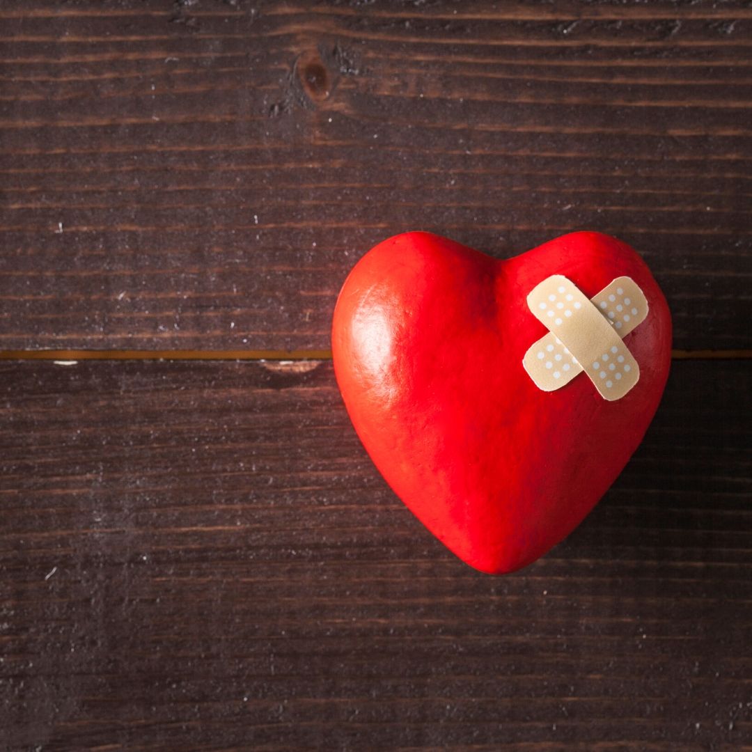 A red 3D heart with two plaster in a cross-shape on a wooden background