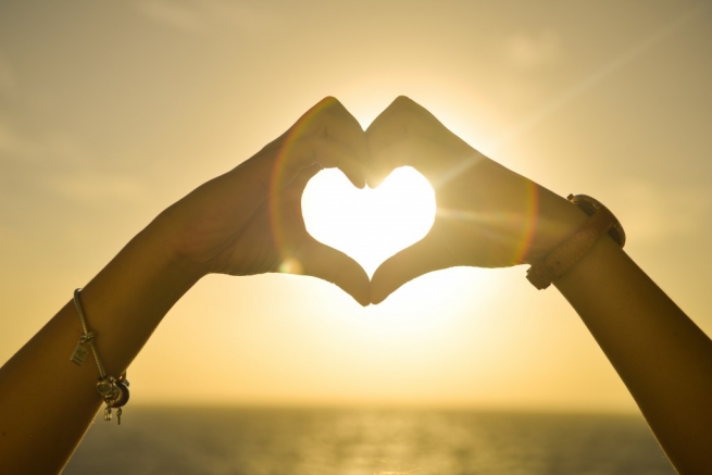 A women making a love heart with her hands, with the sea in the background