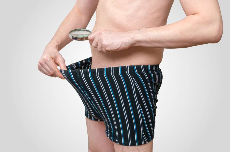 a man wearing striped boxers looking at his private parts with a magnifying glass