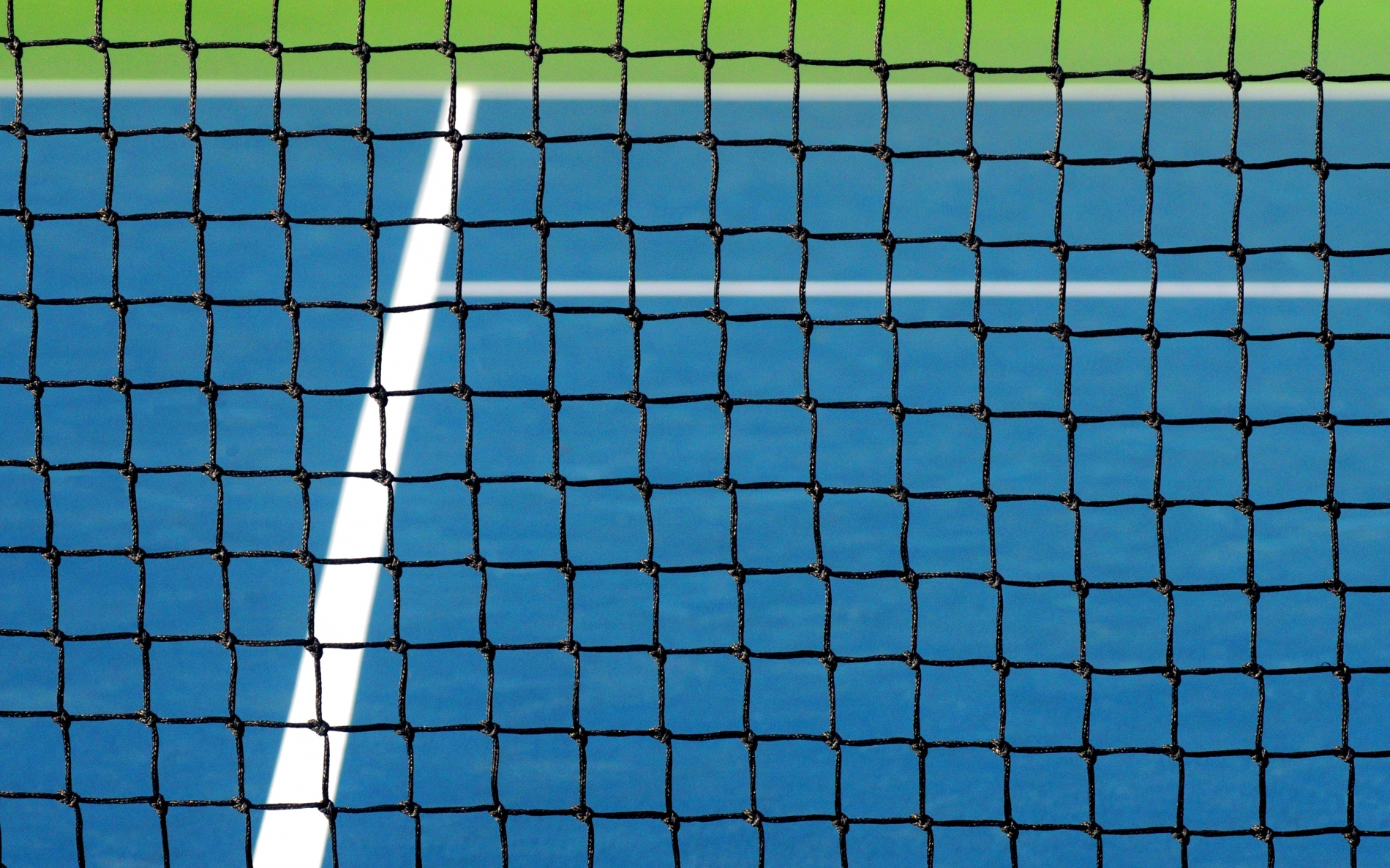 A blue tennis court with white lines looking through the black netting