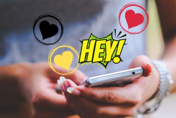 two hands with long natural coloured nails holding a mobile phone are in focus, around this are red, yellow and black doodled hearts with "Hey" written abouve it.