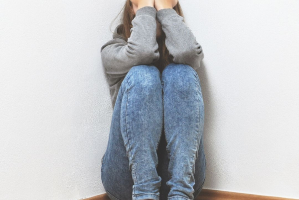 A woman crouched in the corner with her knees drawn up and her hands over her face clearly upset