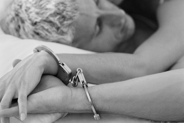 Black and white image of two people in bed with one wrist each in a set of handcuffs