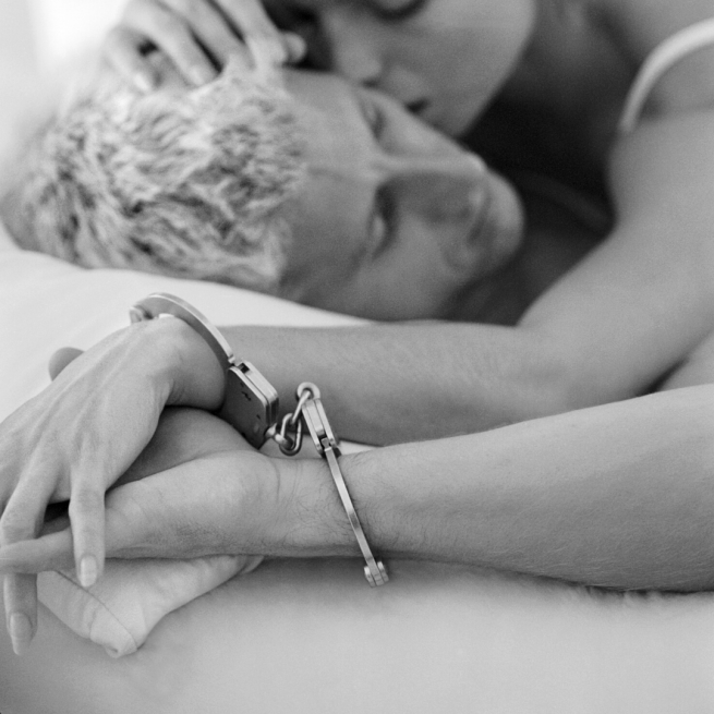 Black and white image of two people in bed with one wrist each in a set of handcuffs