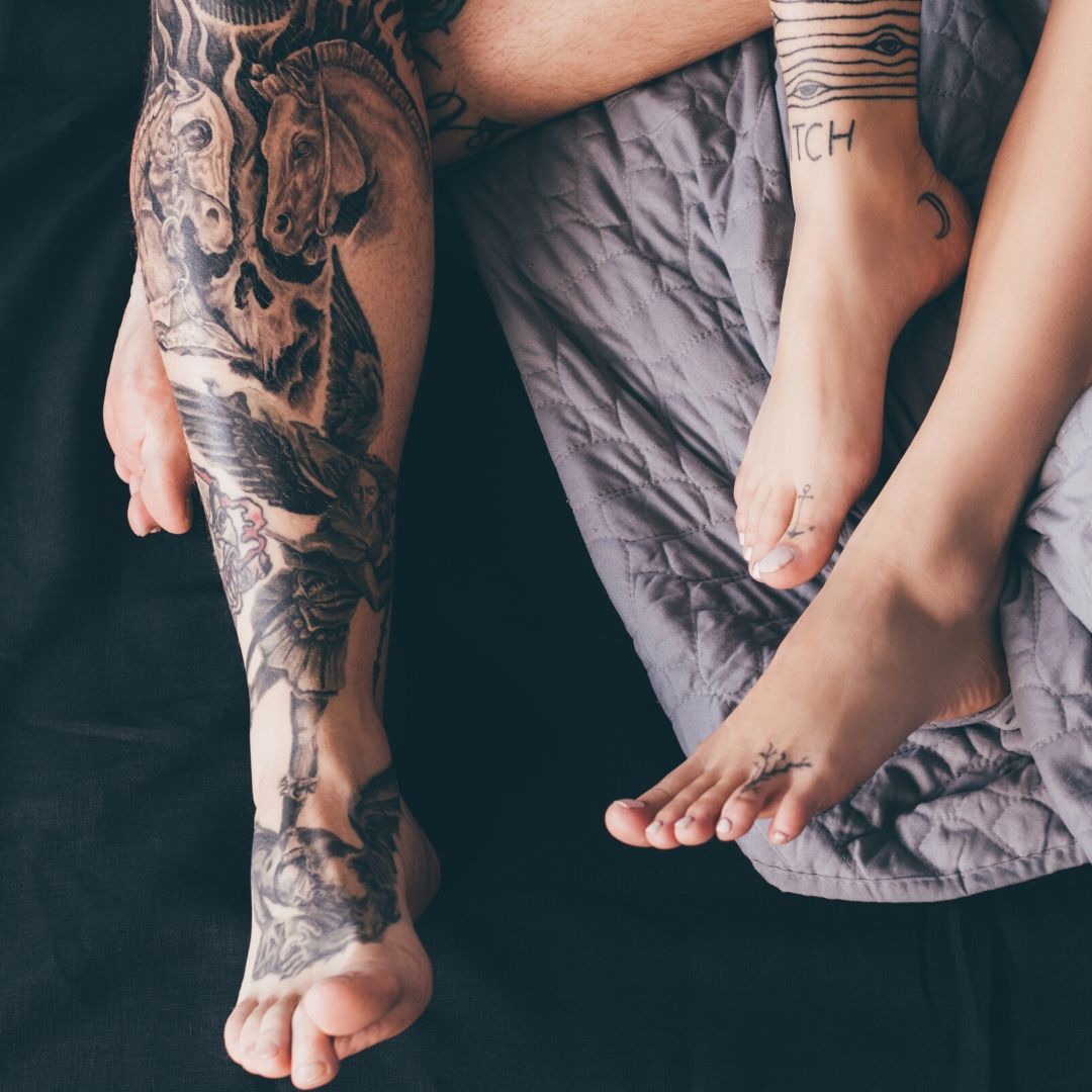 The tattoed legs and feet of a couple lying on a bed