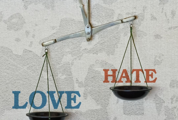A set of scales hanging on a peg against a wall, one says Love the other says Hate