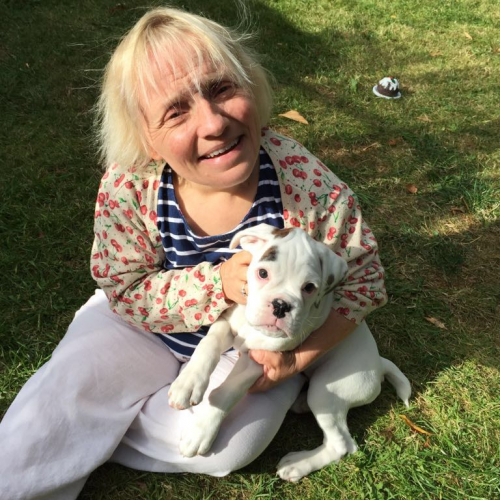 Becky Batten sat on grass cuddling a small white dog.