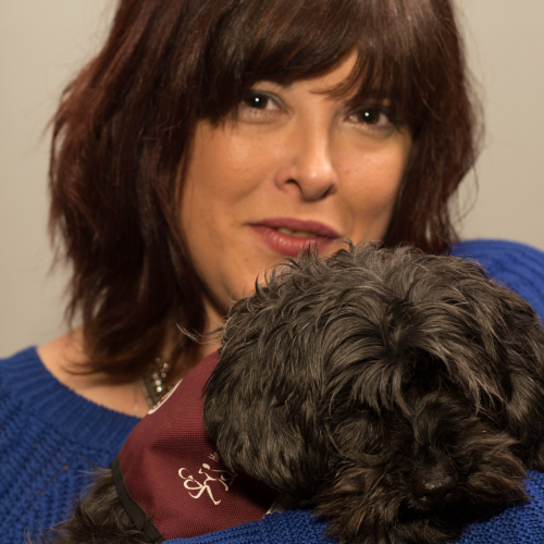 Claire Holland holding a dog with a maroon hearing dog coat on.