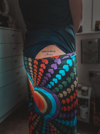 An image of legs wrapped in a pride flag, a flash of left bum cheek is showing where Carley has Enhance The UK and the word Jennie tattooed in black ink