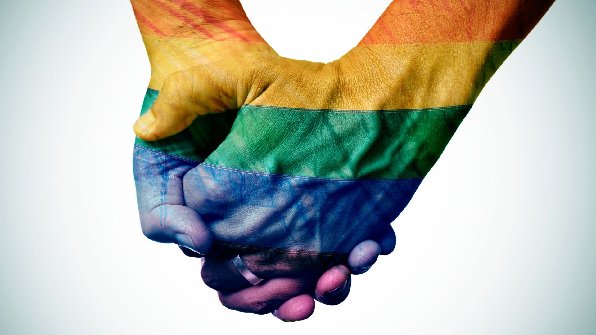 Two hands clasped together with the hands and arms painted in the pride flag