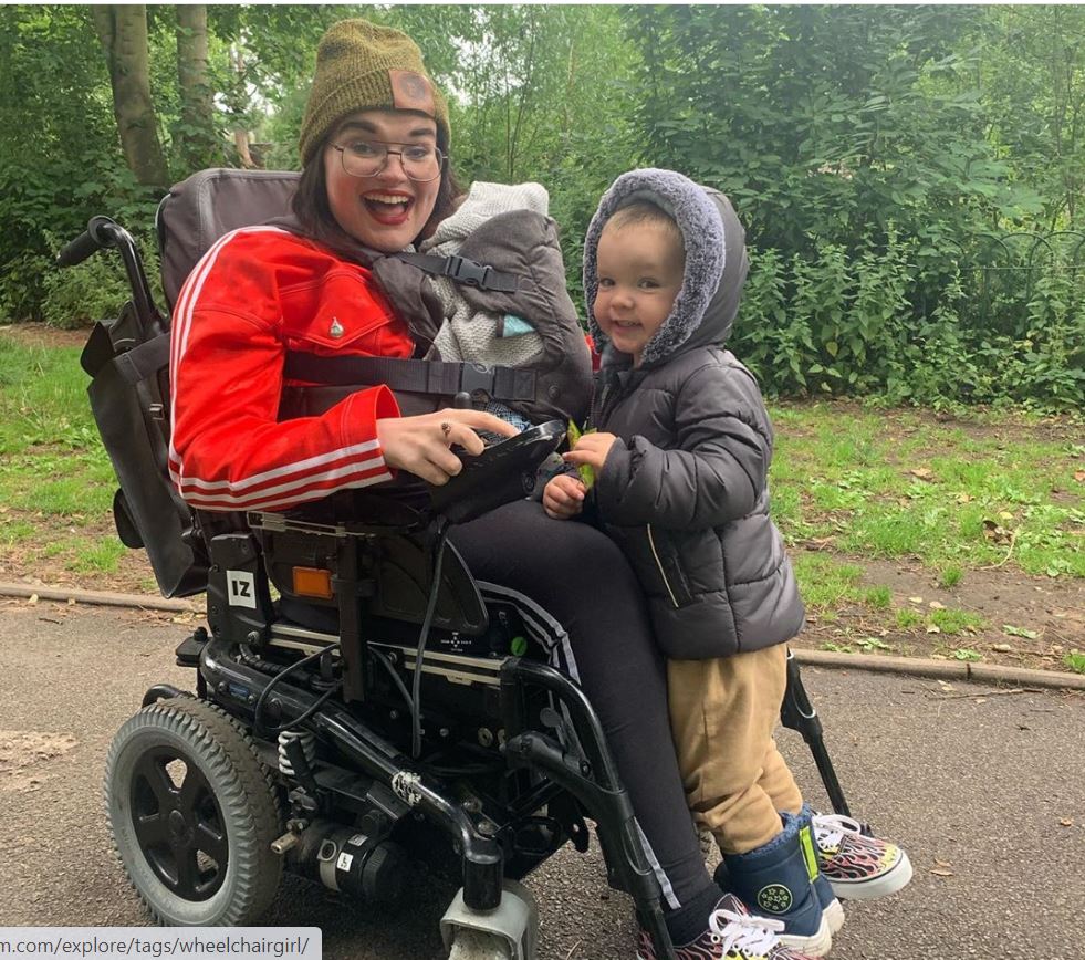 Kelly is pictured in her electric wheelchair with her son Mason and newborn Hunter. She is wearing a bright red adidas top, and is beaming at the camera
