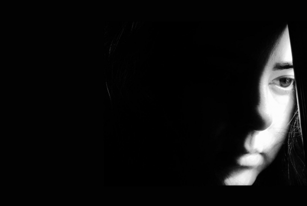 a black and white image with half a face peeking through a black curtain