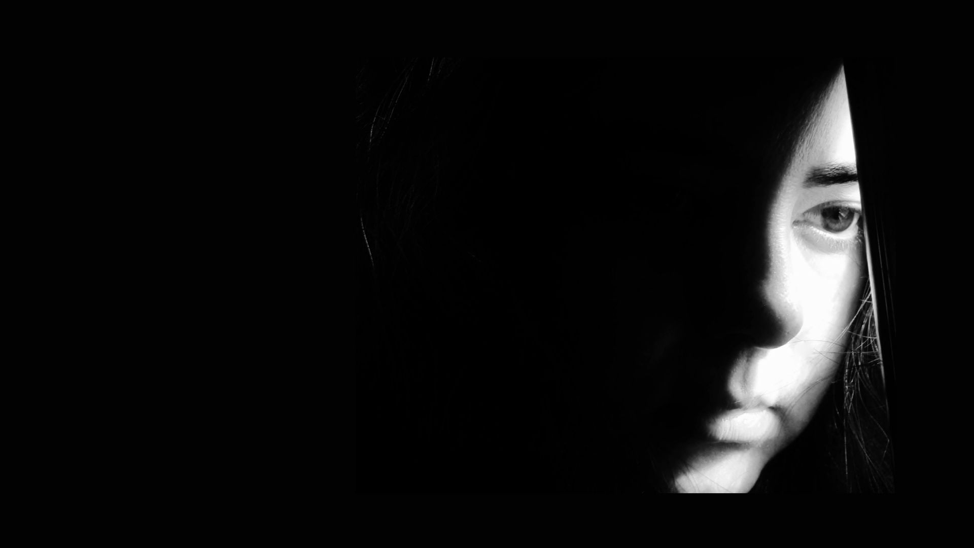 a black and white image with half a face peeking through a black curtain