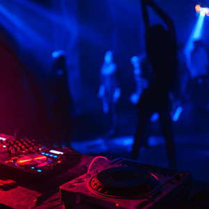 Blue and pink lit image of aa music deck with a dancer in the background