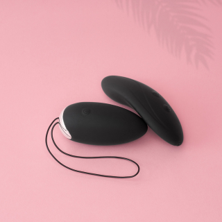 Pink background with the toy in black. It looks similar to a computer mouse in shape 