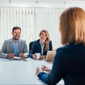 Picture of the back of a ladies head sitting across the desk from a man and a woman in an interview situation