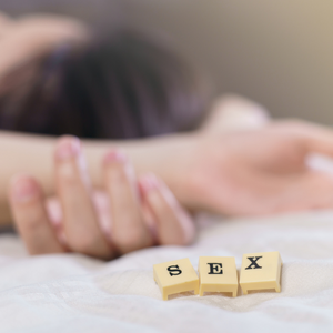 Blurred image of someone lying on a bed. There are scrabble tiles in focus reading sex