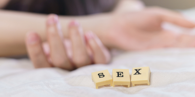 Blurred out images of people on a bed with scrabble tiles in focus reading sex
