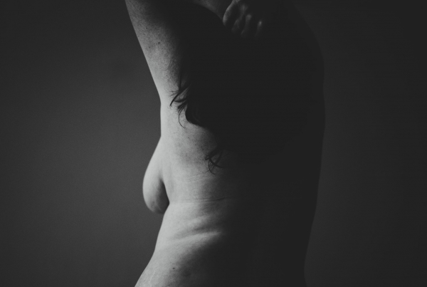 An black and white image of a person, naked with their arms in a posed position above her head