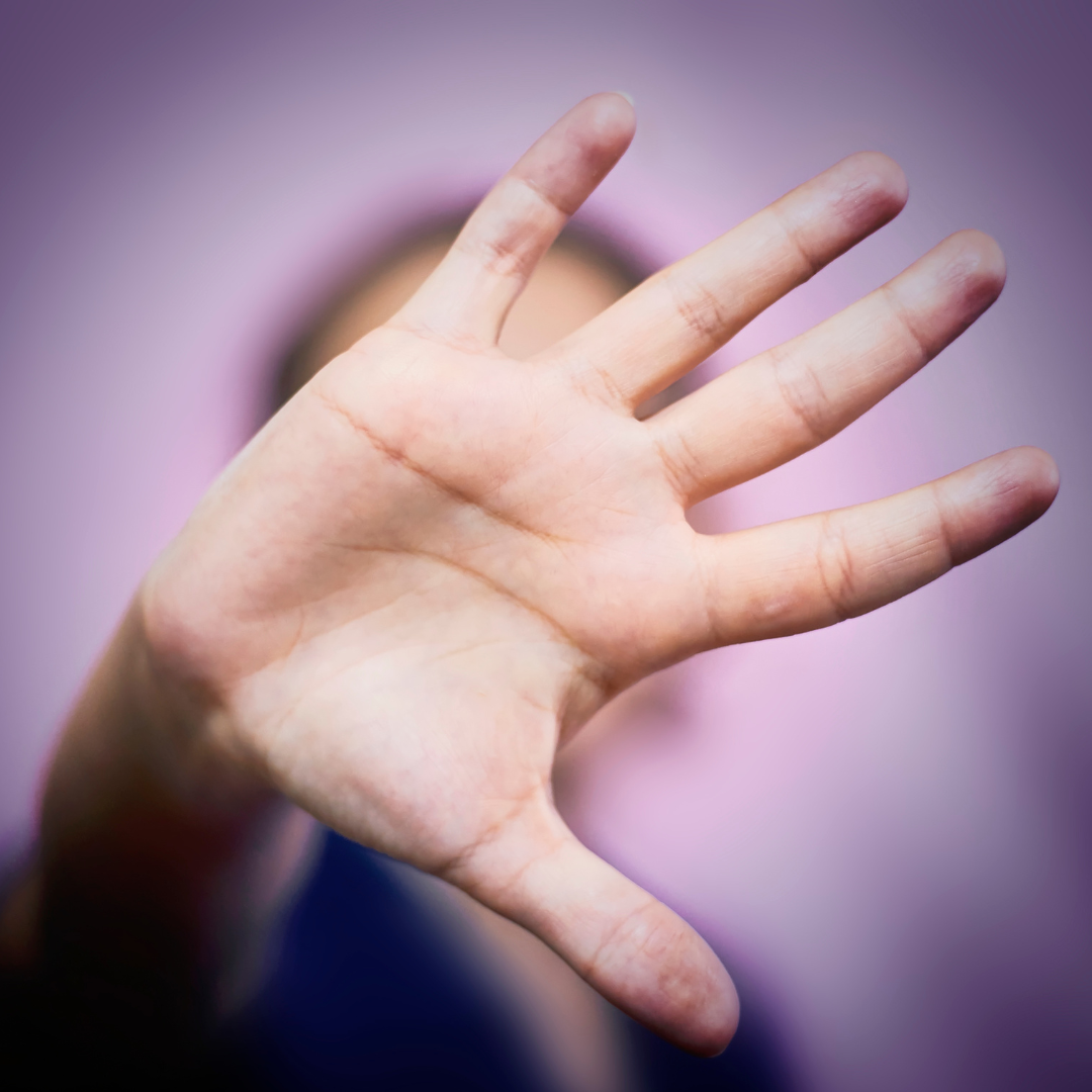 A person stood with the palm of their hand facing outward, covering their face. With a purple background