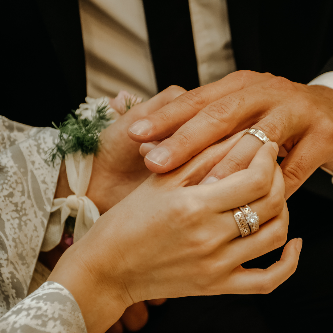 close up photograph of two people putting their wedding rings on each other hands