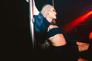 Sex positive party: A drag artist with long blonde hair spins around a pole in a dark nightclub