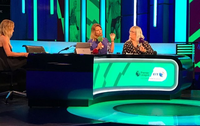 Three women seated at a brightly lit television studio set with blue and green neon-style lighting.