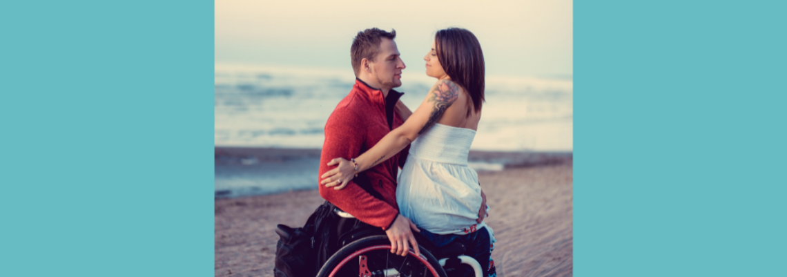 A woman sits on a man's lap. The man is sitting in a wheelchair. They are looking into each other's eyes.