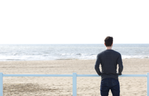 A man stands with his back facing the camera, he is looking out at the sea.