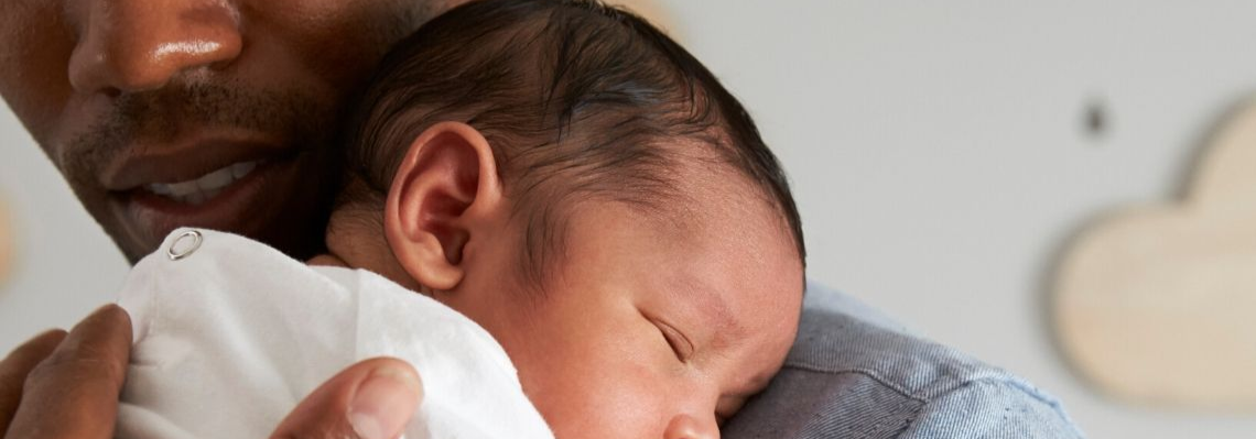 A parent holding his child. The child's head is resting on the parent's shoulder.