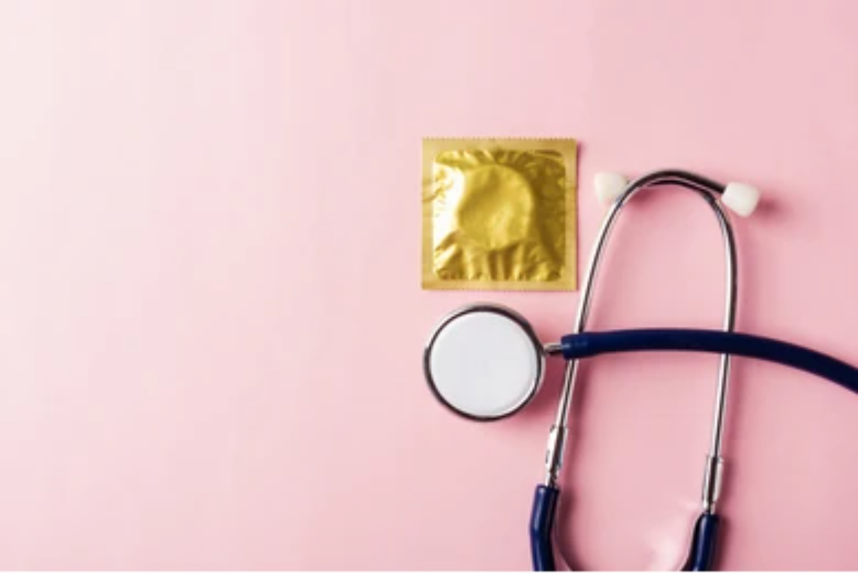 A condom and a stethoscope against a pastel pink background.