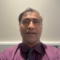 A headshot of Jignesh. He is wearing a burgundy shirt and a blue tie with white spots. He is lit from above.