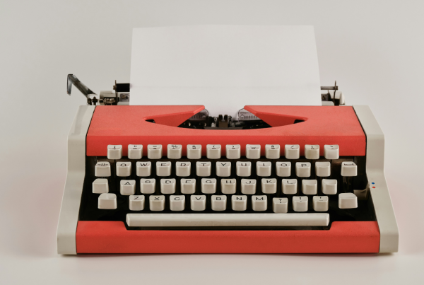 A red and black typewriter with one single sheet of white paper