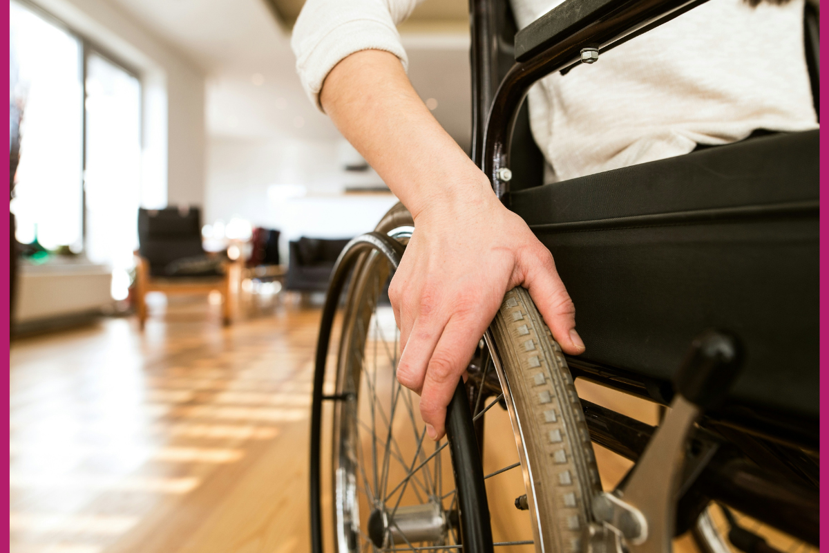 Disability and friendship: A person using a wheelchair. A close up of their hand on the wheel of the chair with a room in the background