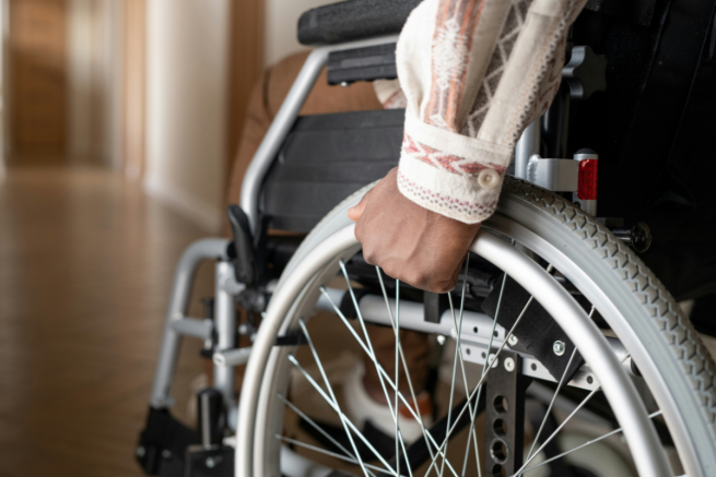 Accessible Shelters: a person has their hand on the wheel of a wheelchair while facing a long corridoor. We cannot see their face. Only their hand