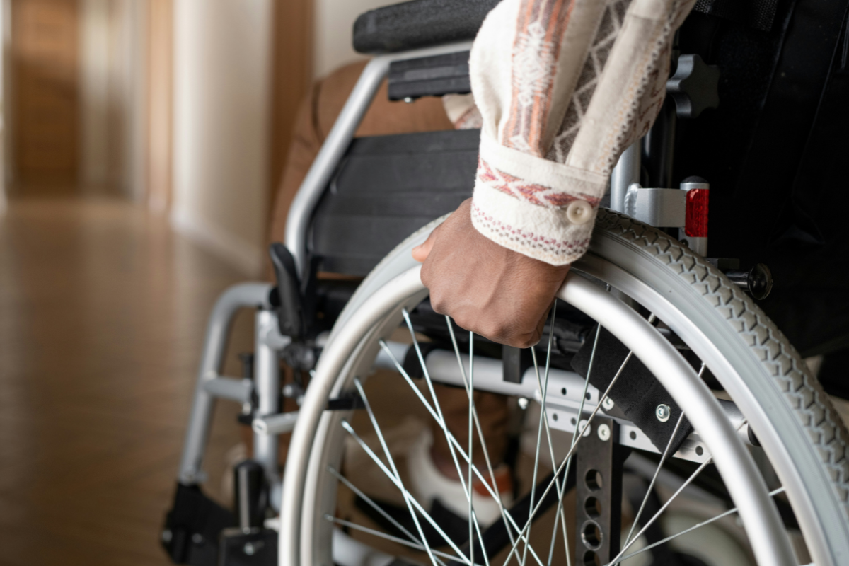 Accessible Shelters: a person has their hand on the wheel of a wheelchair while facing a long corridoor. We cannot see their face. Only their hand