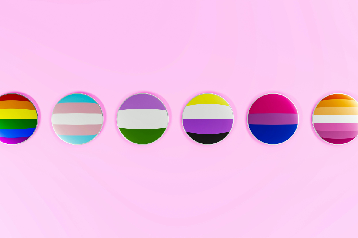 A row of LGBT+ flags as pins. There is a rainbow, trans flag, a sexual flag, non binary, bisexual and lesbian badge in a row