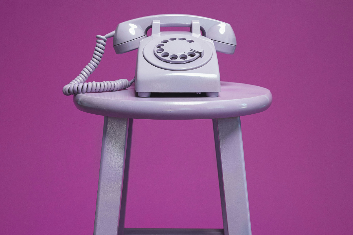 A lavender dial phone on a lavender wooden stool.