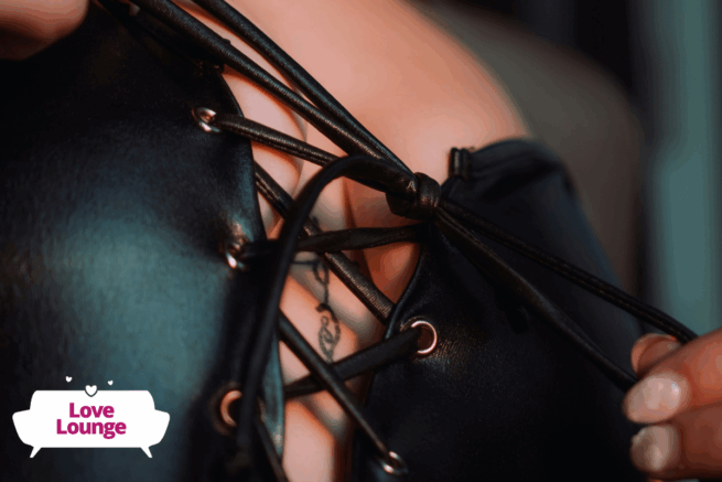A person is pulling the strings of a black PVC top closed over their breasts